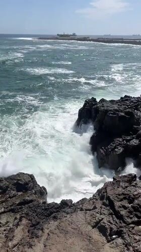 Waves crash against rocky Arica coastline under clear skies