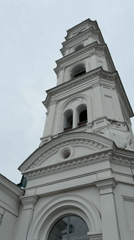 White bell tower with green domes observed under overcast sky