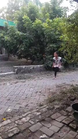 A young girl is running down a brick pathway past a motorcycle and a building.