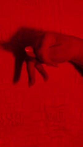 The video shows a hand in a red-lit environment, followed by a series of indistinct objects or shapes against a red background. The shapes and objects remain unclear due to the red lighting and overall blurriness.