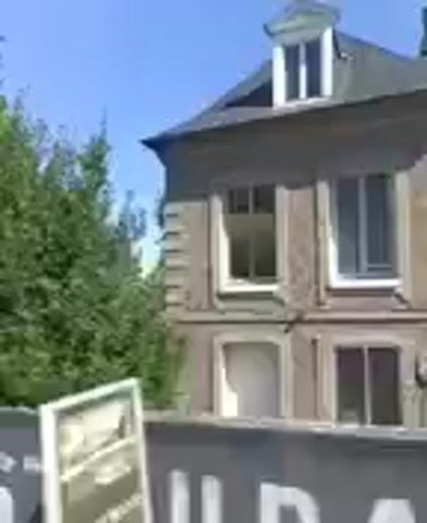 This is a blurry, low-resolution video of a car driving down a road lined with trees. The sky is blue. There are some buildings visible through the trees. There are no people clearly visible in the video. The video quality is very poor and it is difficult to make out any specific details.