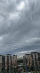 Aircraft formation flies over urban area amid cloudy skies