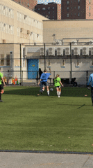 Young adults play soccer on NYC field amid nearby construction