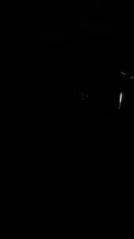 A very dark video shows a body of water with a reflection of lights on the right side. In the distance, there are a few small green lights visible. The overall scene is very dark and indistinct.
