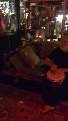 The video shows a group of people dancing inside a dimly lit room. The room is illuminated with red light and some other colored lighting. The people appear to be enjoying themselves, moving to music, although specific details about the music are unavailable. A red patterned rug is visible on the floor. Some furniture is visible in the background. The overall setting resembles a casual social gathering or a party.