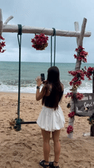 Woman photographs ocean at decorated beach swing in Thailand