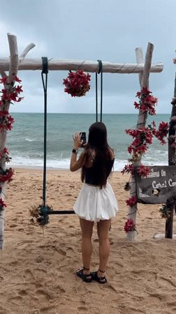 Woman photographs ocean at decorated beach swing in Thailand