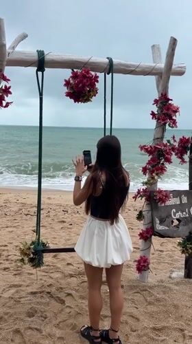 Woman photographs ocean at decorated beach swing in Thailand