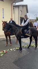 Four riders on horseback travel flower-lined street in Italy