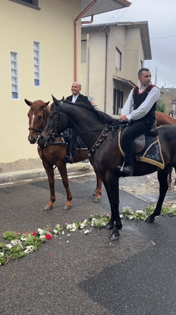 Four riders on horseback travel flower-lined street in Italy