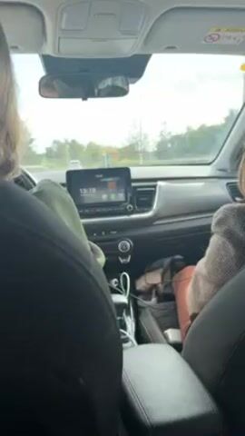 The video shows the interior of a car driving on a road. Two people are visible in the front seats, but their faces are not clearly seen. The driver has long hair, and the passenger is wearing a grey coat. The dashboard features a digital display showing the time as 13:20 and the date as February 24, 2024. The car passes a bus stop on the side of the road where a person is sitting. The general environment appears to be outdoors during the day.