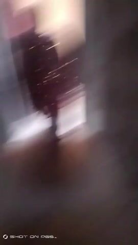 The video shows a person walking, wearing a magenta-colored saree with glitter or sequins. The camera follows behind them, offering a view of their feet and the lower portion of the saree as they walk down a corridor or hallway. The walls are light peach or tan, and the floor appears to be concrete or stone, slightly textured. The video is somewhat shaky and the focus is not always sharp. The words "SHOT ON PES_" are visible in the lower left corner of the frame.