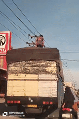 Man stands atop truck as woman follows on scooter