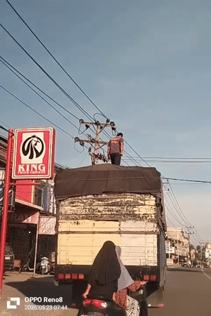 Man stands atop truck as woman follows on scooter