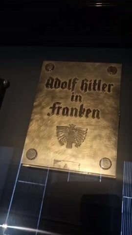 The video shows a display case containing a gold-colored box with the inscription "Adolf Hitler in Franken" and a German eagle emblem. The box has four circular decorations at each corner. The camera then pans to a display card providing information about the box in German and English. The description indicates the box is a casket titled "Adolf Hitler in Franken" and describes it as a gift to Adolf Hitler. Another similar box is described as a box with a Silesian eagle gifted to Adolf Hitler.