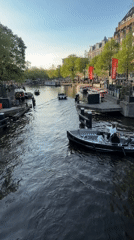 Boats navigate Amsterdam canal during evening golden hour