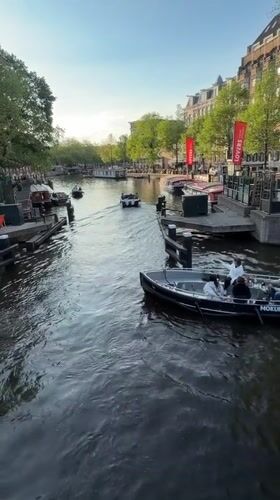 Boats navigate Amsterdam canal during evening golden hour