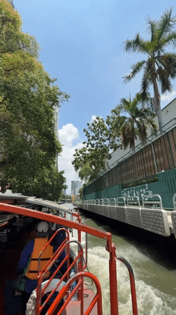 Red passenger boat navigates Bangkok canal on sunny morning