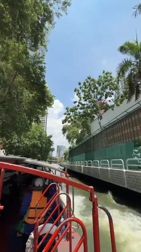 Red passenger boat navigates Bangkok canal on sunny morning