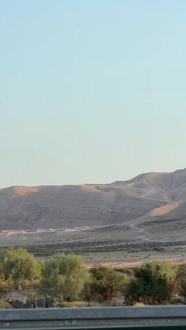 The video shows a landscape with mountains and vegetation in the background. In the foreground, there is a power line tower with electrical equipment. The sky is clear and blue.
