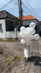 Woman with balloons and flowers walks through Kuta Selatan