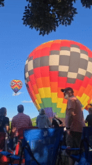 Colorful hot air balloons lift off at an outdoor gathering
