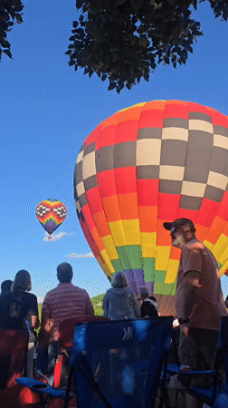 Colorful hot air balloons lift off at an outdoor gathering