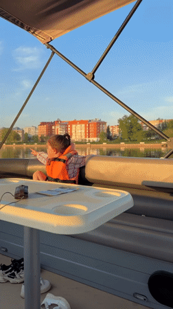 Child in life vest explores calm lake from pontoon boat