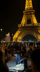 Street musician draws crowd performing near illuminated Eiffel Tower