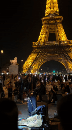 Street musician draws crowd performing near illuminated Eiffel Tower