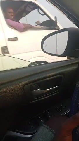 The video, taken from inside a car, shows a first-person perspective of driving on a road. Another vehicle, a white van, is initially to the side and then in front of the camera car. The driver's hands are visible on a blue steering wheel cover. The dashboard displays a warning message: "Maintenance Required." The road is wide and lined with streetlights. The sky appears hazy. Briefly, a person is seen walking along the side of the road.