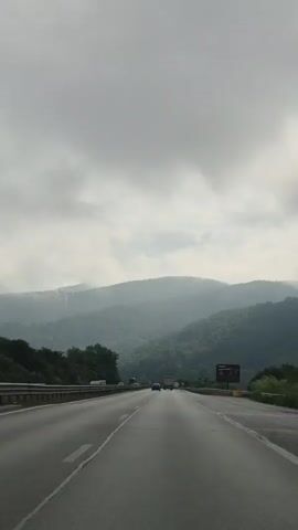 This media file captures a scenic view from a car driving on a highway in Churek, Bulgaria. The subject is the highway itself, stretching into the distance, with rolling, tree-covered mountains forming the backdrop. The sky is overcast and cloudy, suggesting a day with diffused light, possibly with fog or mist adding to the atmospheric depth of the mountains.

Several vehicles are visible on the highway, indicating ongoing travel. On the right side of the road, a billboard advertisement is present, though the text is not clearly legible in this resolution. The overall mood is one of transit and contemplation, perhaps a bit somber due to the cloudy weather, but also serene, appreciating the natural landscape. The time of day appears to be daytime, given the visibility and the nature of highway traffic. The setting is clearly a mountainous region, characterized by the lush green slopes and the winding road.