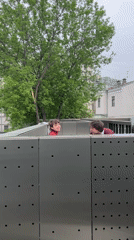 Two young people observed behind gray barrier structure