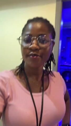 A woman wearing glasses and a pink t-shirt is shown from the chest up in the first shot. She turns to the right and walks forward in the subsequent shots, revealing her jeans and a lanyard with a device attached. The background is dimly lit with blue lighting.