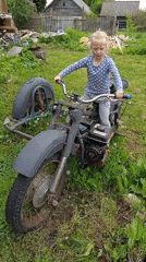 Child plays among abandoned motorcycles and flower gardens in rural Russia