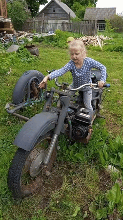 Child plays among abandoned motorcycles and flower gardens in rural Russia