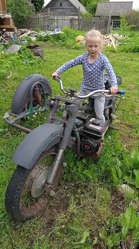 Child plays among abandoned motorcycles and flower gardens in rural Russia