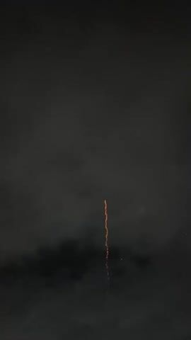 The video shows a fireworks display against a dark, cloudy sky. The first frame shows a single trail of light ascending, which then explodes into a burst of orange sparks. Subsequent frames capture the dissipation of this burst, revealing multiple smaller, white sparks and smoke. The fireworks are in the upper center of the frame, with dark clouds forming the lower portion of the scene. The display is brief, with each frame capturing a distinct moment of the explosive light show.