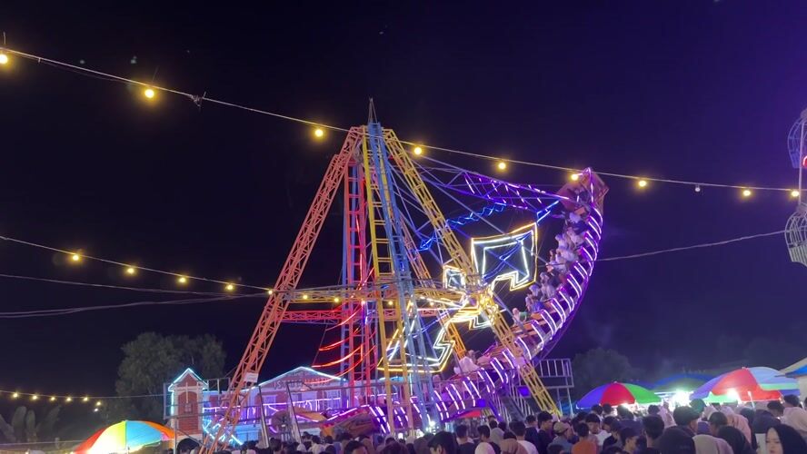 Night market bustles with seafood vendors, carnival rides