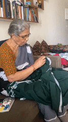 Elderly woman hand-sews green fabric on Chennai couch