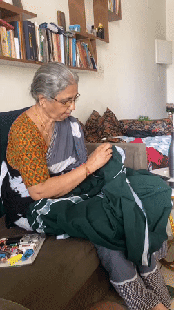 Elderly woman hand-sews green fabric on Chennai couch