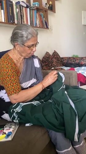 Elderly woman hand-sews green fabric on Chennai couch