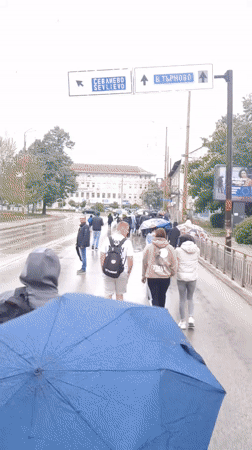 Pedestrians with umbrellas navigate wet streets in Gabrovo