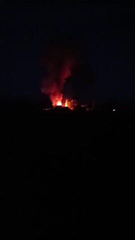 This media file depicts a nighttime scene of a large fire in Didovychi, Ukraine. The primary subject is the conflagration itself, characterized by intense orange and red flames erupting upwards and a thick plume of dark smoke billowing into the night sky. The fire appears to be consuming structures, as evidenced by the visible outlines of buildings or other objects silhouetted against the flames.

The setting is an open area, likely rural or semi-rural, given the silhouette of the horizon which suggests trees or low structures. The time of day is clearly nighttime, with the darkness of the sky contrasting sharply with the brightness of the fire. There are no discernible weather conditions mentioned, but the smoke indicates active burning.

The activity taking place is a significant fire, possibly an uncontrolled blaze or an explosion followed by a fire. The scale of the fire suggests it could be a structure fire, a vehicle fire, or even a wildfire. The emotions conveyed by the image are those of alarm and destruction, due to the destructive nature of fire.

There is no visible text within the media file. The overall impression is one of chaos and emergency.