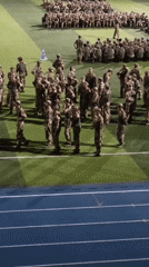 Military cadets drill in formation on a floodlit stadium field