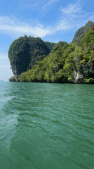 Boat navigates island channel near cave entrance in Krasom