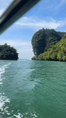 Boat navigates island channel near cave entrance in Krasom