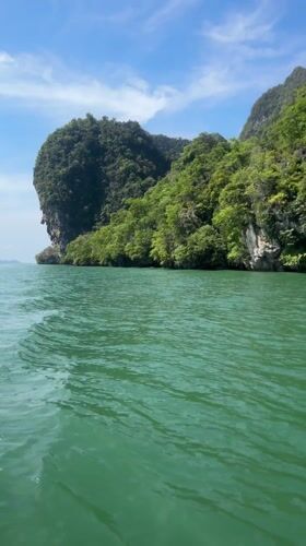 Boat navigates island channel near cave entrance in Krasom