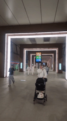 Pedestrians traverse illuminated hallway with high ceilings, rectangular lighting