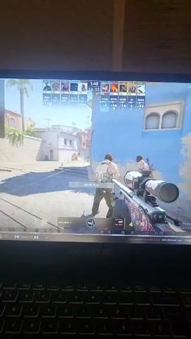 Here's a detailed description of the video:

The video shows someone playing Counter-Strike: Global Offensive (CS:GO) on a GIGABYTE laptop. The player is using an AWP sniper rifle, aiming down the sights in a sunny, outdoor environment within the game. The player successfully eliminates two opponents with headshots. The game interface shows the score, player information, and in-game currency. The environment appears to be a Mediterranean-style setting with stucco buildings. The video captures the first-person perspective of the player and their in-game actions.